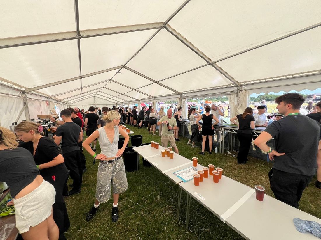 Busy festival bar marquee with staff serving and pints lined up